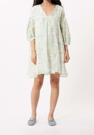 Woman wearing a loose, knee-length white dress with pastel geometric lines and three-quarter puffed sleeves, paired with light blue ballet flats.