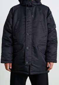 Chaqueta de invierno negra acolchada con cierre de botones y cremallera, bolsillos frontales con solapa y un bolsillo con cremallera en la manga izquierda.