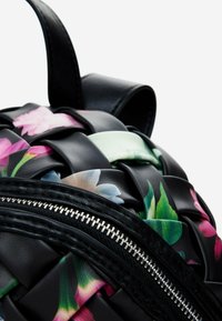 Mochila tejida negra con acentos florales en rosa y verde, con una textura suave y detalle de cremallera plateada a lo largo del lado.