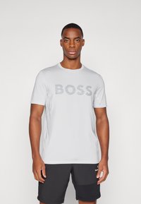 Lys grå kortermet t-skjorte med en stor grå "BOSS"-logo. Laget av glatt stoff, med rund hals og minimale sømdetaljer.
