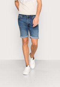 Mörkblå denimshorts med vikta fållar, med en klassisk femficksdesign och dragkedja fram. Kombination med vita sneakers.