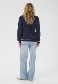 Marineblauwe sweatshirt met ribgebreide boorden en zoom, gecombineerd met lichtblauwe wijde jeans. Glad materiaal met een casual pasvorm, zonder zichtbare patronen of accenten.