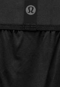 Melna auduma ar savilkšanas tekstūru, ar logo etiķeti augšpusē un šuvēm gar malām.