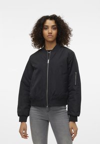 Czarna kurtka bomberka o gładkiej fakturze, z przednim zamkiem błyskawicznym, ściągaczami na rękawach oraz kieszenią na zamku na lewej rękawie. Klasyczny krój, lekka konstrukcja.