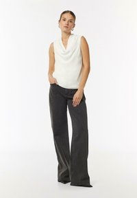 Biała bluzka bez rękawów z kołnierzem w stylu cowl, zestawiona z ciemnoszarymi dzwonami z srebrnymi drobinkami i delikatnym połyskiem.