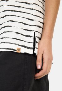 Czarno-biała koszulka w paski, wykonana z miękkiego materiału, z bocznym rozcięciem i małą skórzaną metką na dolnym brzegu.