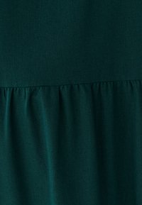 Tamsiai žaliai mėlynas audinys, pasižymintis lygiu paviršiumi, su raukšlėtu apatiniu kraštu ir struktūruota viršutine dalimi. Matomų raštų ar aparatūros nėra.