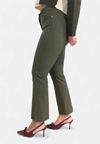 Olijfgroene nauwsluitende broek met een rechte pijp en metalen details, gecombineerd met bordeauxrode slingback hakken van lakleer met een strikdetail.