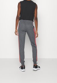 Harmaat collegehousut, joissa punaiset sivuraidat ja joustava vyötärönauha, kapea malli. Mustat lenkkitossut valkoisilla pohjilla. Yksinkertainen muotoilu, svetari ei näy.