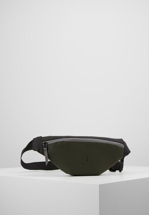 Olive green and black waist bag with front zipper pocket and adjustable black strap displayed on white pedestal.