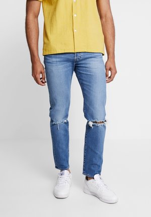 Lichtblauwe denim jeans met versleten knieën, gecombineerd met een gele button-up shirt en witte sneakers. Casual pasvorm.