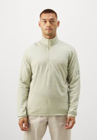 Hele roheline, lukuga pullover, mis on valmistatud pehmest kangast, millel on kõrge krae. Omab pikki varrukaid ja peeneid õmbluse detaile. Sobib beežide pükste juurde.