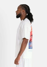 Witte katoenen t-shirt met korte mouwen, voorzien van een kleurrijke grafische print op de achterkant, die een landschap met tekstuele elementen toont.