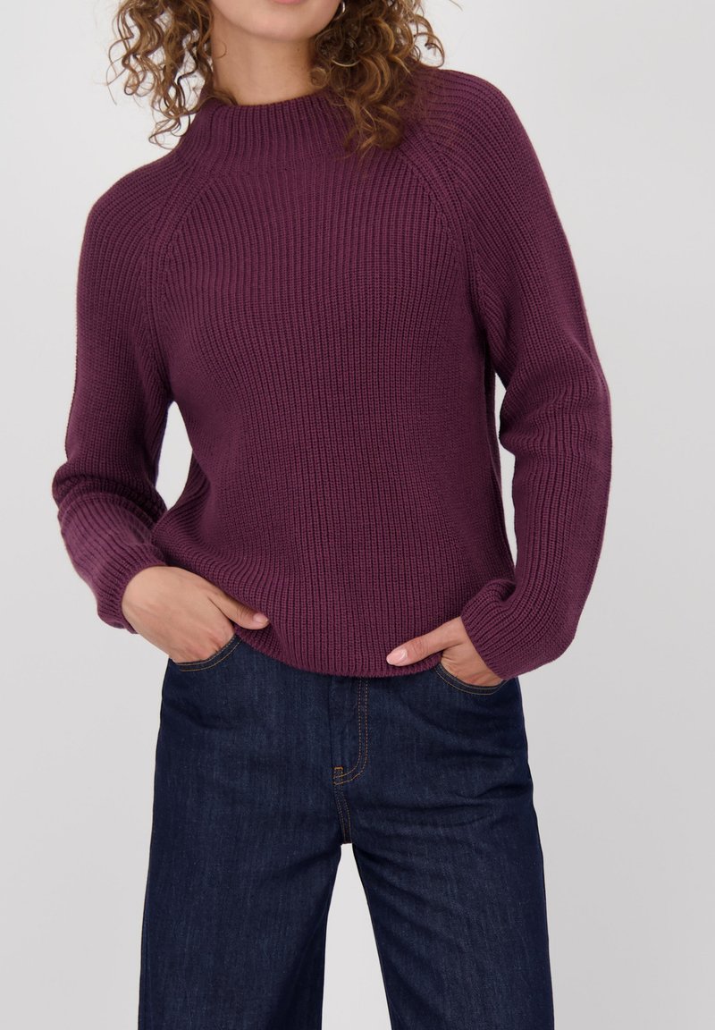 Paarse, geribde gebreide trui met een hoge hals en lange mouwen. Gecombineerd met donkerblauwe, iets losse spijkerbroeken.
