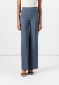 Weite Hosen aus strukturiertem blauen Stoff. Mit hohem Bund und Seitentaschen, kombiniert mit schwarzen Riemchensandalen.