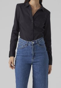 Camicia nera con bottoni, realizzata in tessuto liscio, caratterizzata da maniche lunghe e colletto strutturato, abbinata a jeans in denim blu a vita alta.