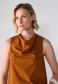 Rustfarvet ærmeløs top med draperet cowl-halsudskæring, glat tekstur og løs pasform. Minimalistisk design uden synlige mønstre.