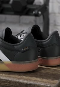 Black leather athletic shoes with a white stripe, textured surfaces, and a translucent rubber sole featuring a gradient from orange to pink.