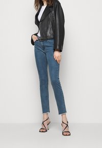 Svart lädercropped jacka över en vit t-shirt, tillsammans med blå skinny jeans och svarta remsandaler med en liten klack.