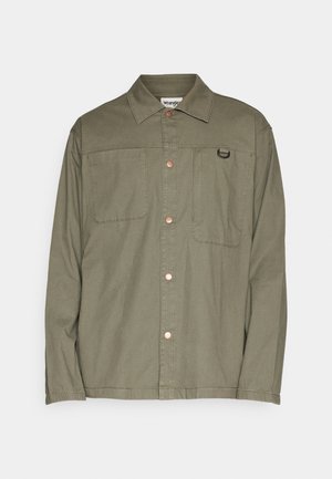 Chemise olive en coton avec texture lisse, dotée de deux poches poitrine et d'accents en métal couleur cuivre.