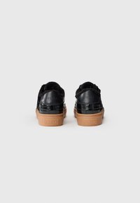 Une paire de baskets noires doublées de fourrure avec des semelles en caoutchouc marron, vue de l'arrière, présentant le logo Furla sur le talon et la semelle.