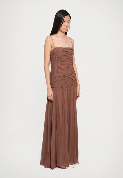 Brown, floor-length dress with ruched texture, thin spaghetti straps, and a flowing skirt. Made of lightweight fabric for soft drape.