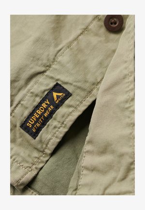 Groen utility shirt met een geweven stof, knoopsluiting en een zwart label met gele tekst "SUPERDRY UTILITY WEAR."