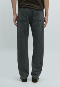 Ciemnoszare dżinsy denimowe o prostym kroju nogawki, z tylnymi kieszeniami i subtelną fakturą. Noszone z ciemną koszulą i czarnymi butami.