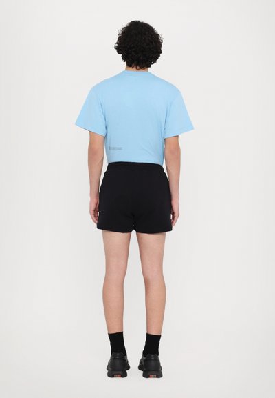Himmelblaues T-Shirt mit kurzen Ärmeln, schwarze Shorts und schwarze Schuhe. Das T-Shirt hat ein kleines Textdetail über dem Saum. Schlichte, lässige Passform.