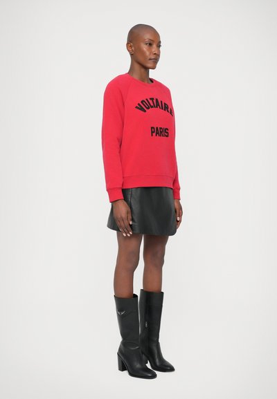Rode sweatshirt met "VOLTAIRE PARIS" in zwart, gecombineerd met een zwarte leren minirok en zwart leren kniehoge haklaarzen. Glad textuur.