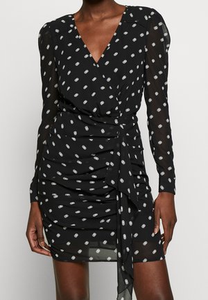Czarna sukienka kopertowa w białe groszki, z długimi, przezroczystymi rękawami, marszczoną spódnicą i wiązaniem w talii.