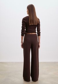 Ruskean neulotun kahden osan asu, jossa on tiukasti istuva pitkähihaisa paita ja korkeavyötäröiset leveälahkeiset housut. Tasainen pinta koko asussa.