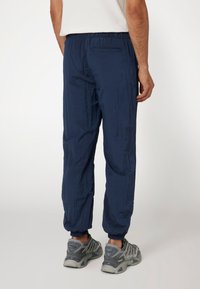 Tamsiai mėlynos lengvos kelnės su elastinga juosmena, turinčios tekstūruotą apdailą ir pasagų apačioje. Slim fit su užpakaline kišene.