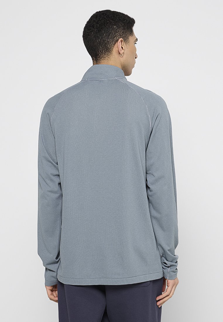 Camiseta deportiva de manga larga en un ligero tono gris, hecha de un tejido transpirable. Presenta un cuello y mangas ranglán con una textura suave.