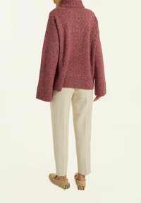 Übergroßer bordeauxfarbener Pullover mit hohem Kragen, strukturierter Strickmuster und gerippten Bündchen, kombiniert mit cremefarbenen tapered Hosen und beigen Slippern.