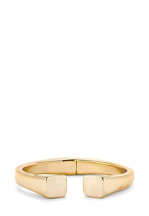 Brazalete abierto en metal dorado pulido, con un diseño minimalista que presenta extremos cuadrados y una textura suave y continua.