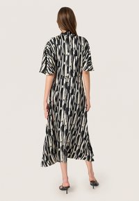 Black and cream patterned dress with short sleeves, flowing A-line shape, and high neckline. Smooth texture and mid-calf length.