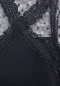 Svart nätplagg med detaljerad spetskant och prickmönster, med ett slätt svart baslager som framhäver den lager på lager-designen.