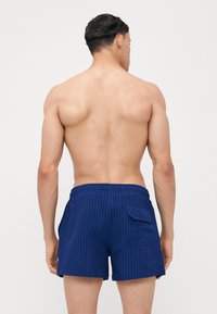 Blå stribede badebukser med elastisk talje og sidelomme, lavet af et let materiale, med et struktureret design.