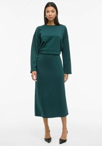 Groene jurk met lange mouwen van zachte stof, met een relaxte pasvorm, een ronde halslijn en een rechte silhouet, gecombineerd met zwarte hakken.