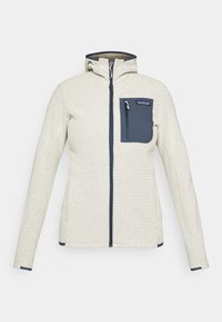 Cremefarbene Jacke mit Struktur, Frontreißverschluss, blauem Reißverschluss-Brusttasche und Kapuze.