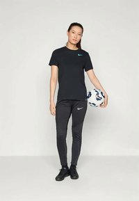 Svart Nike t-skjorte med turkise logoer, paret med svarte treningbukser med teksturerte detaljer. Personen holder en fotball.