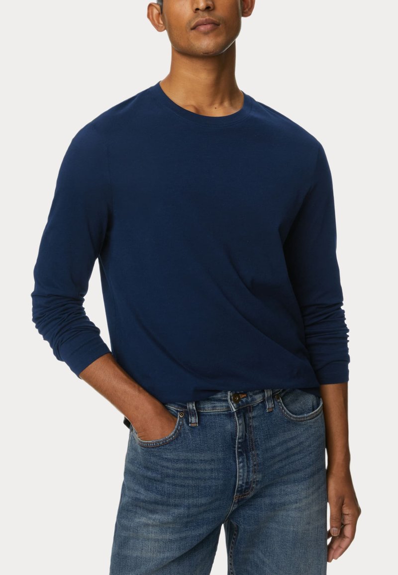 Marineblaues Langarm-T-Shirt aus weichem Stoff, mit Rundhalsausschnitt und enganliegenden Ärmeln, kombiniert mit hellblauen Jeans.