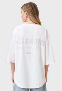 Biała, oversize T-shirt z krótkim rękawem, z napisem "ALLSAINTS" w srebrnym haftem na plecach, zaokrąglonym dołem i luźnym krojem.