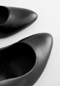 Black leather high-heel shoes with a pointed toe, featuring a smooth texture and a seamless design.