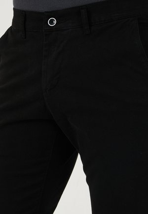 Mustat puuvillapantat, joissa on kapea malli, etutaskut ja yksi nappisulku vyötäröllä. Sileä pinta ja vähäiset yksityiskohdat.