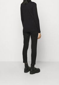 Svart långärmad tröja med en åtsittande design, tillsammans med slim fit svarta byxor. Modellen bär svarta ankelboots, vilket visar en snygg outfit-siluett.