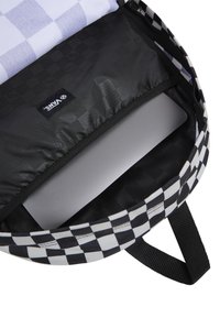 Interno di uno zaino a scacchi bianco e nero con un compartimento imbottito per un laptop, caratterizzato da una superficie grigia liscia e una fodera a motivo scacchiera.