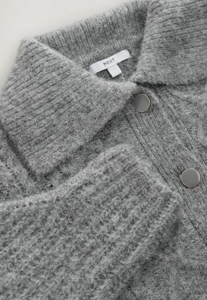 Grauer Strickpullover mit Kragen, ausgestattet mit zwei großen schwarzen Knöpfen und einer strukturierten Oberfläche. Das Markenetikett ist sichtbar.