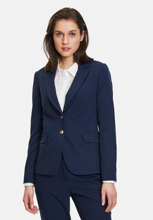 Námořnický modrý blazer se strukturovaným designem, dvěma předními kapsami, zapínáním na jeden knoflík a zlatými prvky. Spárováno s bílou košilí.